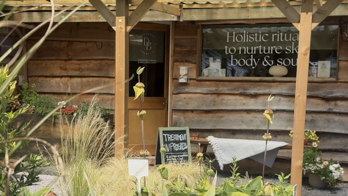 The timber cabin frontage with planting and the window lettering
