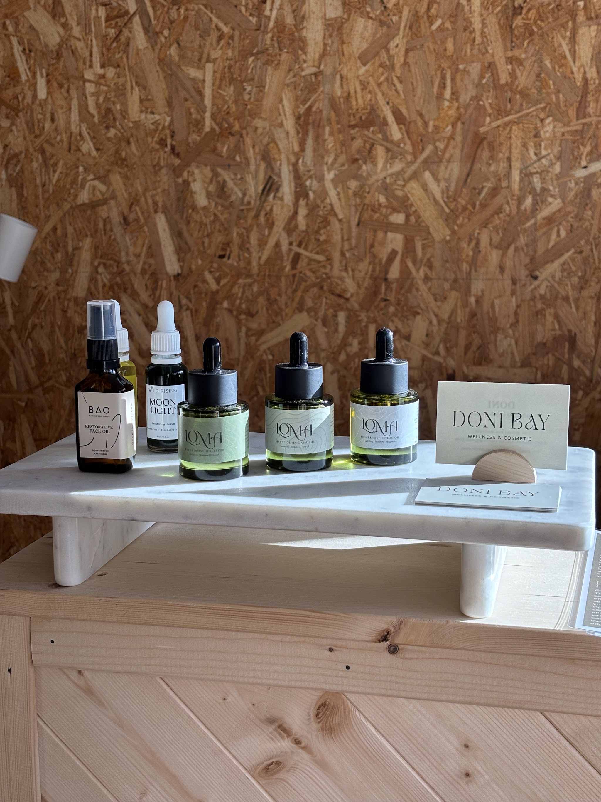 Facial oils on a marble stand beside a Doni Bay card