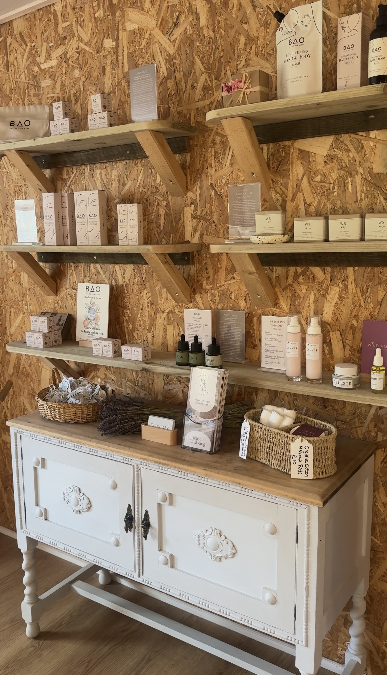Shelves of skincare in the wellbeing shop above a white carved cabinet